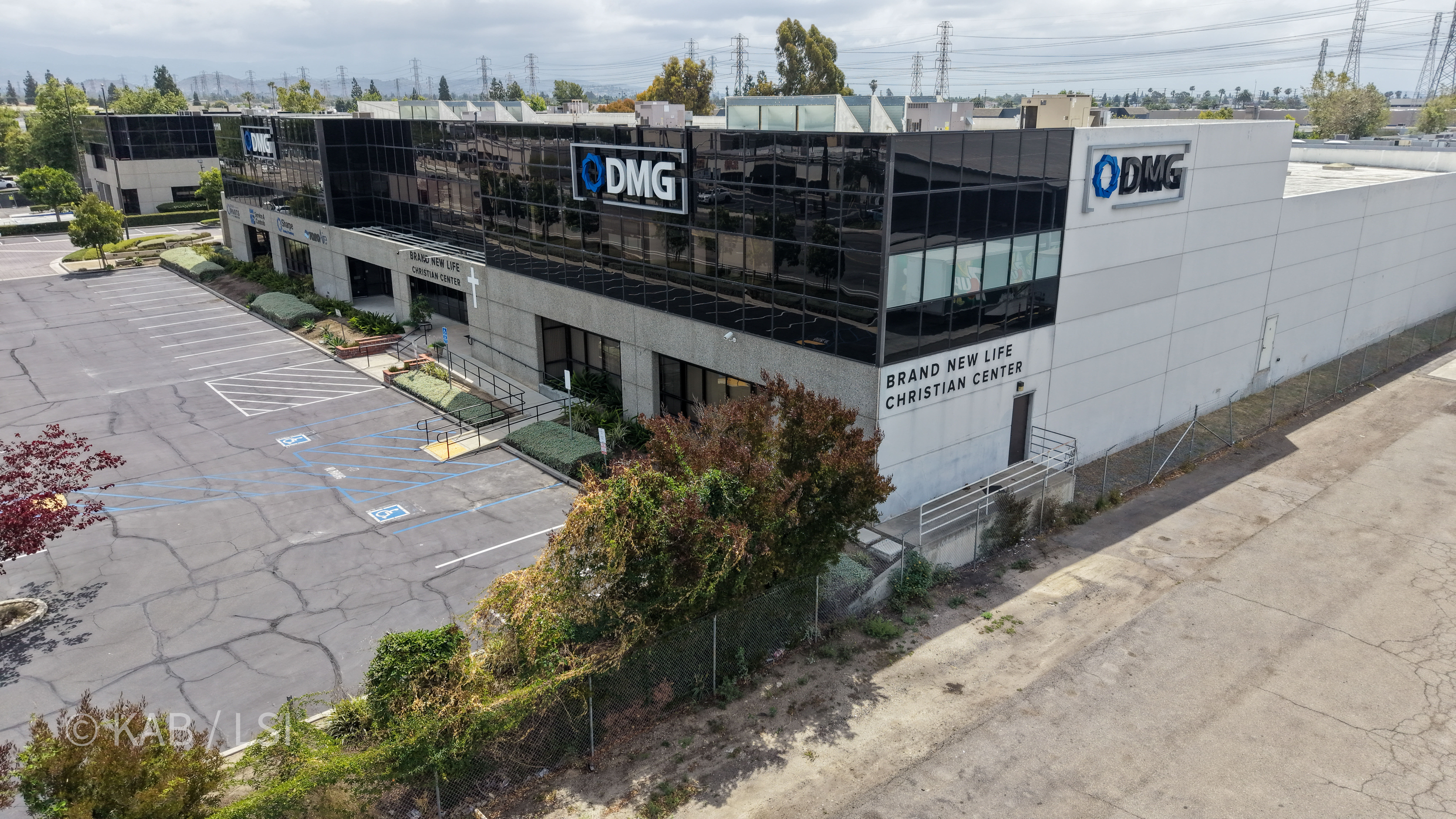 Aerial side view of the 88,000 sq ft building at 1110 W. Taft Ave., Orange, CA, showing DMG HVAC signage and Brand New Life Christian Center signage on the side wall, with the Saddleback foothills in the distance.