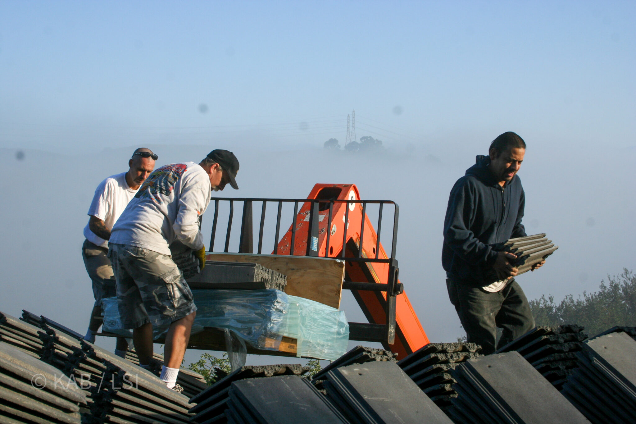 Crew unloading fire-resistant concrete roof tiles in early morning fog on the hills © KAB/LSI