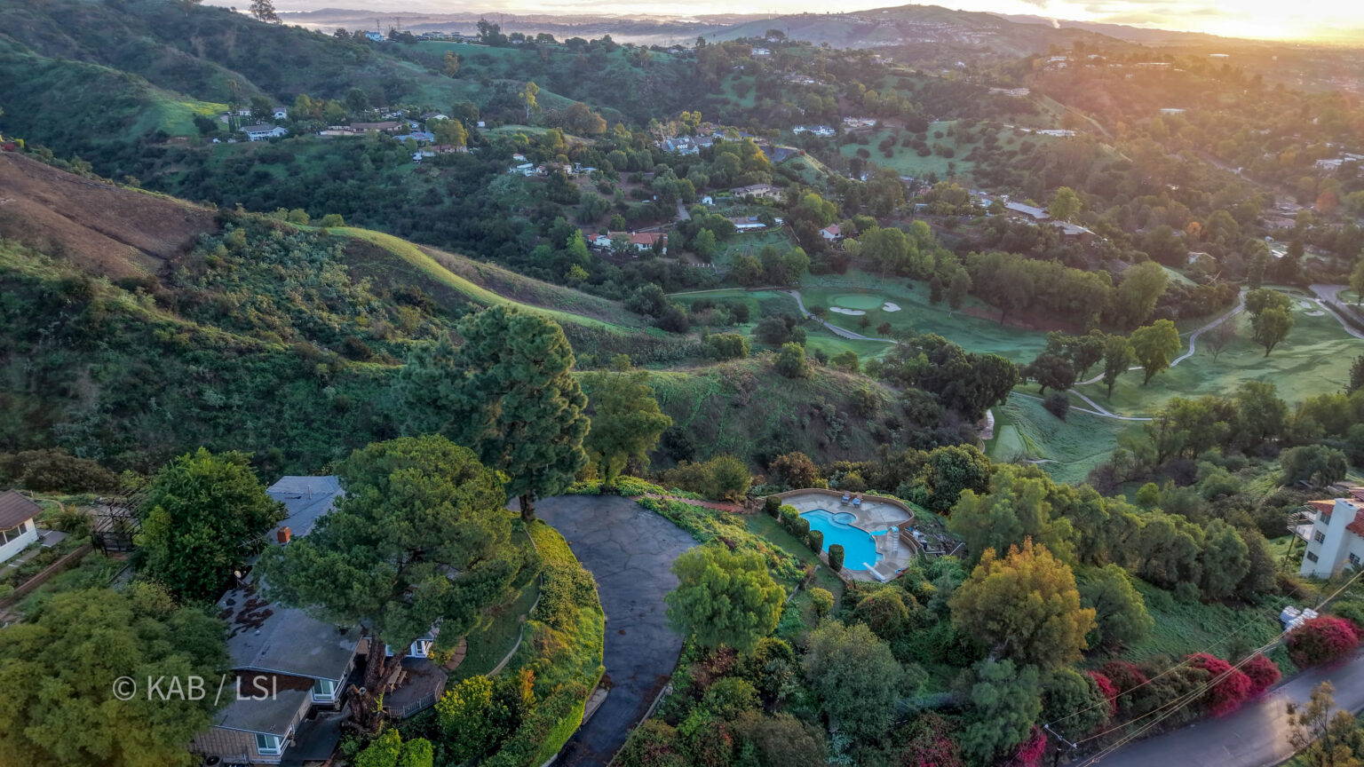 The edge of a La Habra Heights canyon at sunrise, hillside homes among trees with the valley opening below.