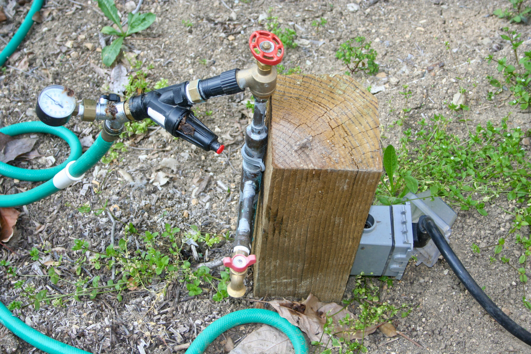 Low-profile Water and Power Station on a La Habra Heights hillside property: pressure-treated post with Type L copper riser, brass inlet valve, pressure gauge, pressure regulator, secondary brass outlet valve, and a weatherproof electrical outlet integrated on the same fixture