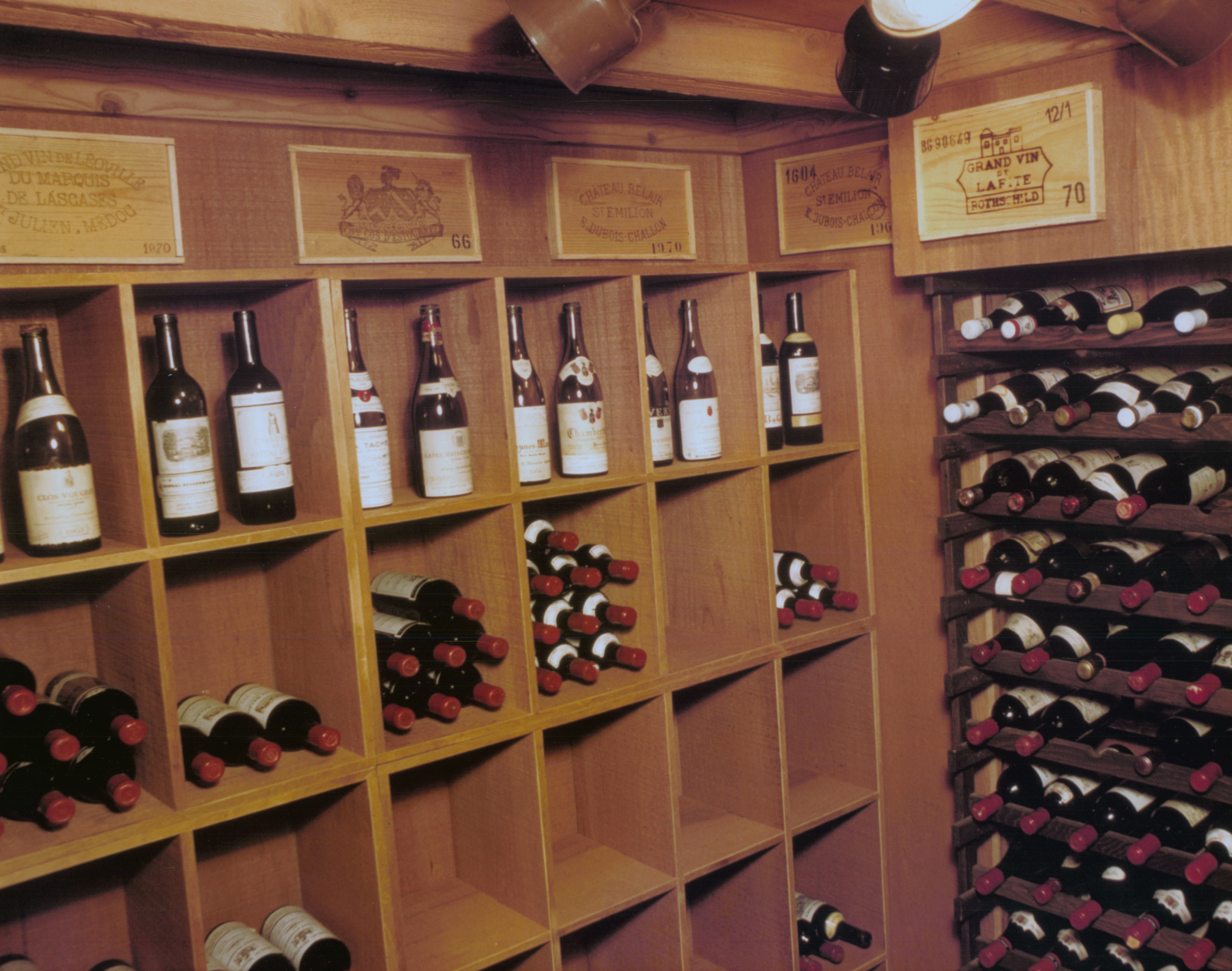 A finished home wine cellar with redwood cube racking, diagonal bottle bins, and an angled display rack full of bottles, wine-crate panels mounted above.