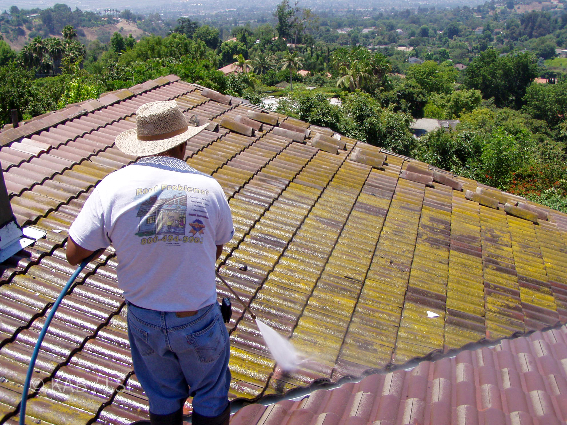 Contractor pressure washing moss from 40 year old clay tile roof on La Habra Heights hillside property with valley view behind