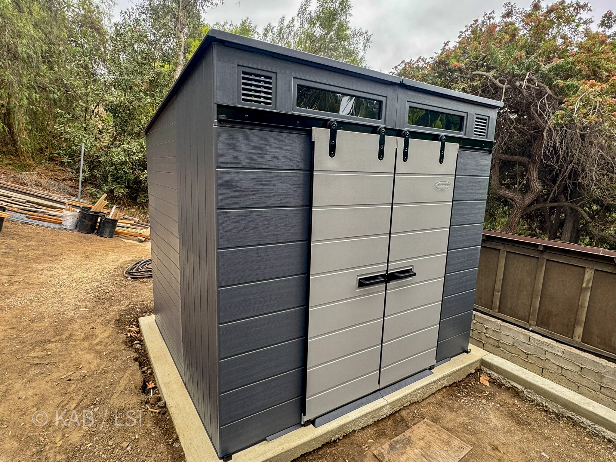 Finished Suncast composite shed installed level on concrete pad LHH hillside property doors aligned floor dry